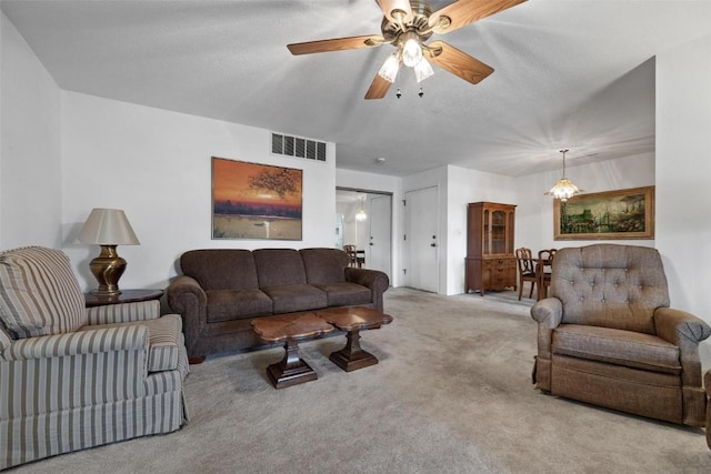 living area featuring a textured ceiling, ceiling fan with notable chandelier, visible vents, and light colored carpet