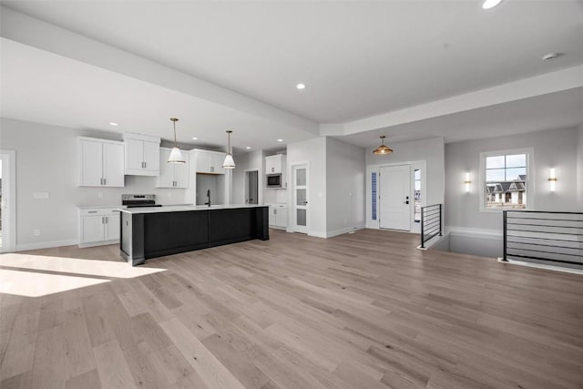 kitchen with decorative light fixtures, sink, white cabinetry, appliances with stainless steel finishes, and an island with sink