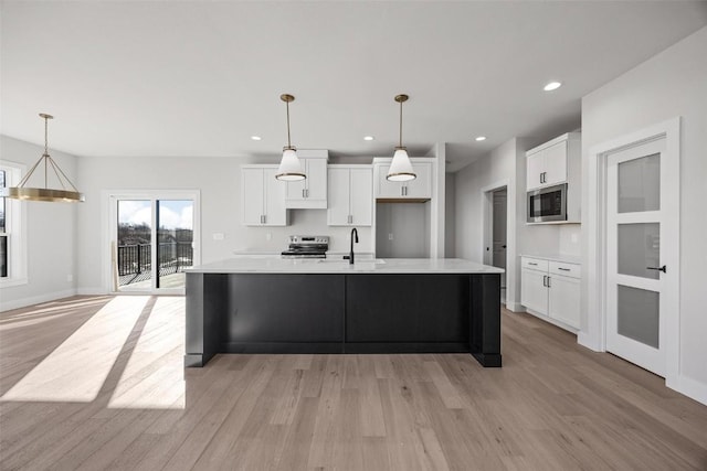 kitchen featuring white cabinetry, electric range, decorative light fixtures, a kitchen island with sink, and built in microwave