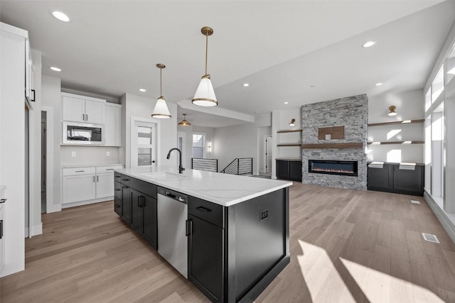 kitchen featuring stainless steel dishwasher, sink, white cabinetry, hanging light fixtures, and an island with sink