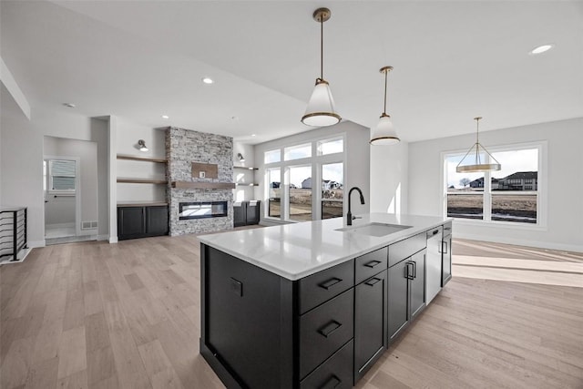 kitchen featuring a center island with sink, light wood-type flooring, a fireplace, pendant lighting, and sink