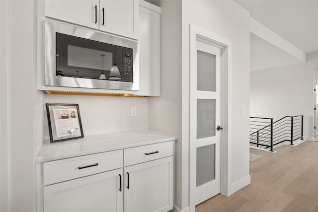 bar featuring baseboards, built in microwave, and light wood-style floors