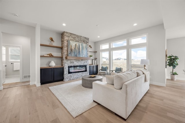 living area featuring a fireplace, visible vents, light wood-style floors, and baseboards