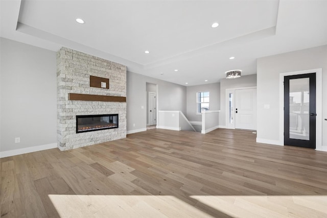 unfurnished living room featuring a raised ceiling, a fireplace, and light hardwood / wood-style flooring