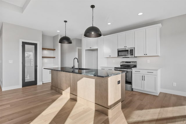 kitchen featuring appliances with stainless steel finishes, light wood-type flooring, white cabinetry, and an island with sink