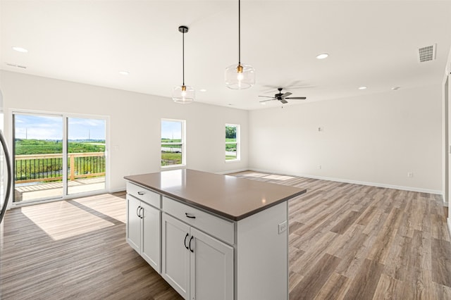 kitchen with white cabinets, light wood-type flooring, decorative light fixtures, ceiling fan, and a kitchen island