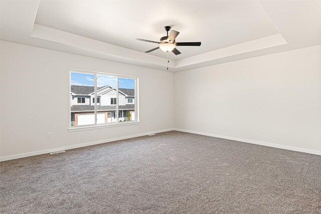 carpeted spare room with a tray ceiling and ceiling fan