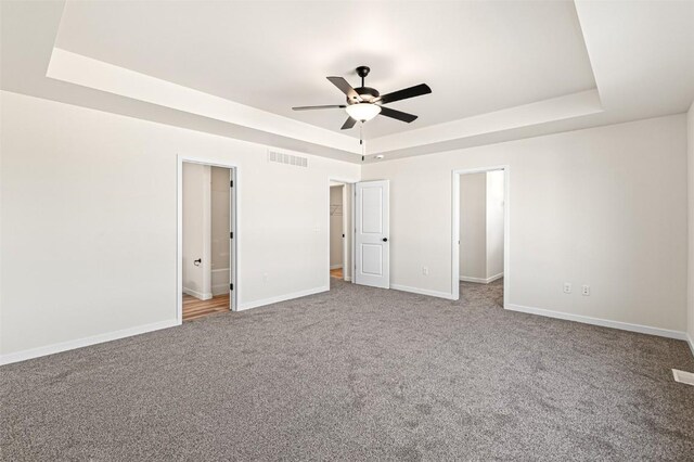 unfurnished bedroom with a raised ceiling, connected bathroom, ceiling fan, and carpet floors