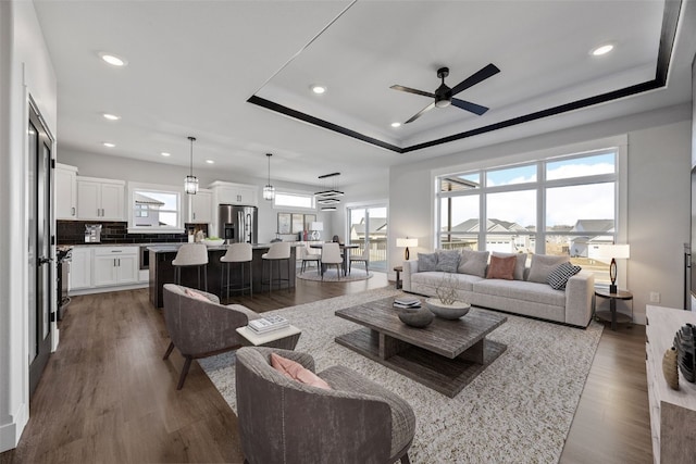 living room with a tray ceiling, dark wood-type flooring, ceiling fan, and plenty of natural light