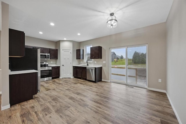 kitchen featuring dark brown cabinetry, sink, hanging light fixtures, light hardwood / wood-style flooring, and stainless steel appliances