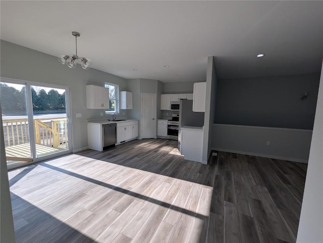 kitchen with dark wood-type flooring, hanging light fixtures, appliances with stainless steel finishes, a notable chandelier, and white cabinetry