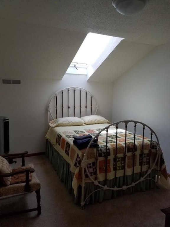 bedroom with vaulted ceiling with skylight, a textured ceiling, and carpet