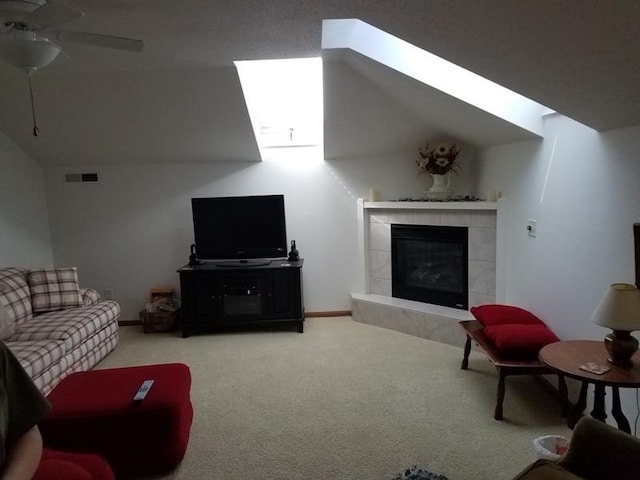 carpeted living room featuring ceiling fan, lofted ceiling with skylight, and a tiled fireplace