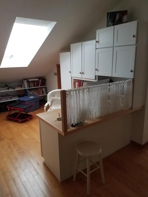 kitchen featuring white cabinets, a breakfast bar, light hardwood / wood-style floors, and lofted ceiling with skylight