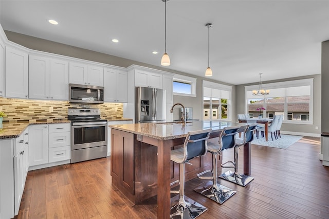 kitchen featuring appliances with stainless steel finishes, pendant lighting, an island with sink, and white cabinets