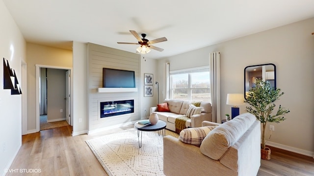 living room featuring a fireplace, ceiling fan, and light hardwood / wood-style floors