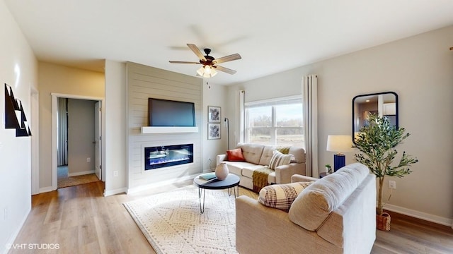 living room with baseboards, a large fireplace, light wood-style flooring, and a ceiling fan