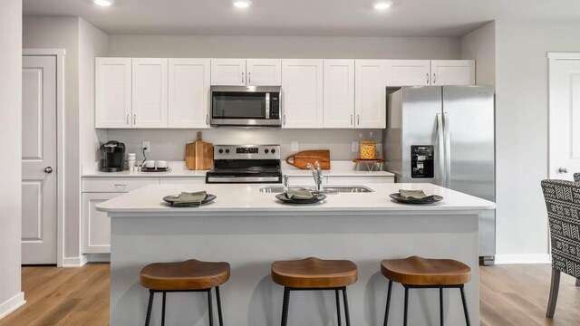 kitchen with sink, light hardwood / wood-style flooring, white cabinetry, stainless steel appliances, and an island with sink