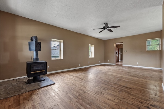 unfurnished living room featuring a textured ceiling, wood-type flooring, ceiling fan, and a wood stove