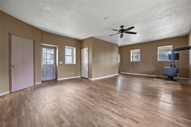 unfurnished living room featuring ceiling fan, a textured ceiling, hardwood / wood-style floors, and a wood stove