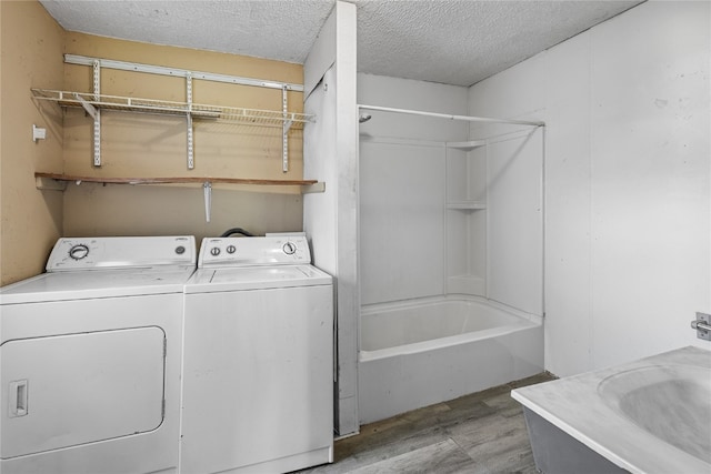 washroom with a textured ceiling, light hardwood / wood-style flooring, and washing machine and dryer