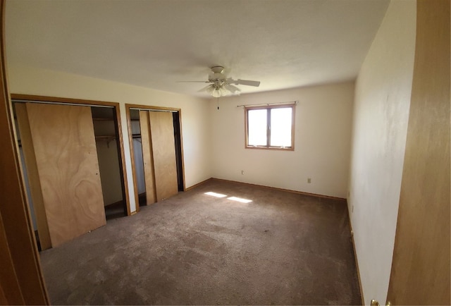 unfurnished bedroom with ceiling fan, two closets, and dark colored carpet