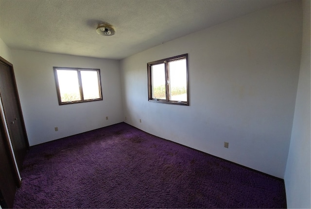 unfurnished room featuring a textured ceiling, dark colored carpet, and a healthy amount of sunlight