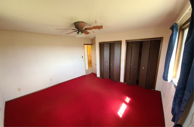 unfurnished bedroom featuring ceiling fan, carpet floors, and two closets