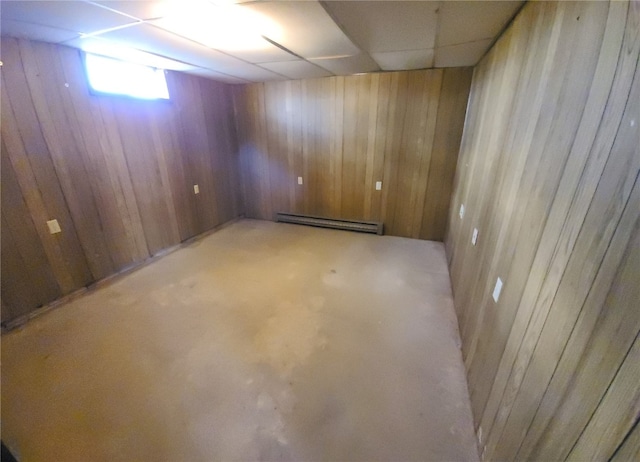 basement with a drop ceiling, a baseboard heating unit, and wooden walls