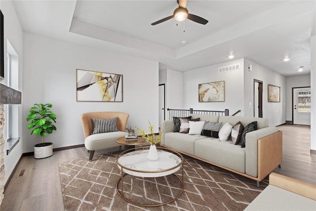 living room featuring ceiling fan, wood-type flooring, and a tray ceiling