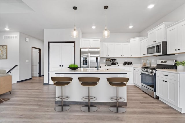 kitchen with hanging light fixtures, a center island with sink, stainless steel appliances, and light wood-type flooring