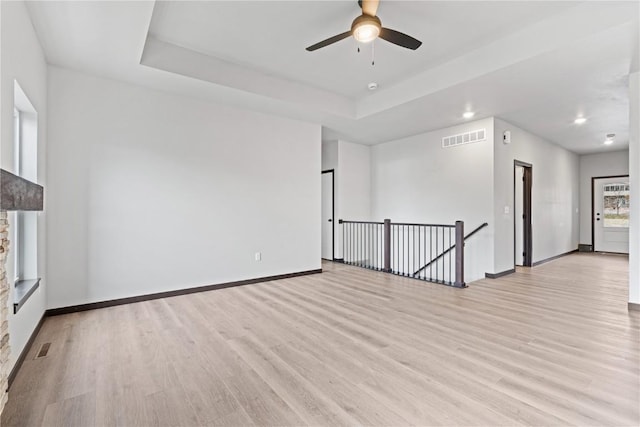 empty room with ceiling fan, a tray ceiling, and light hardwood / wood-style flooring