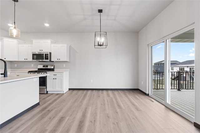 kitchen featuring white cabinetry, sink, hanging light fixtures, stainless steel appliances, and light wood-type flooring