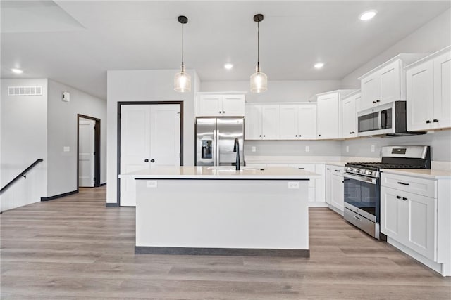 kitchen with appliances with stainless steel finishes, light wood-type flooring, white cabinetry, and a kitchen island with sink