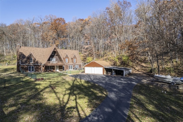 view of front of property with a view of trees, a detached garage, an outbuilding, fence, and a front yard