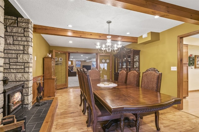 dining area with a wood stove, light wood-type flooring, a textured ceiling, beamed ceiling, and a chandelier