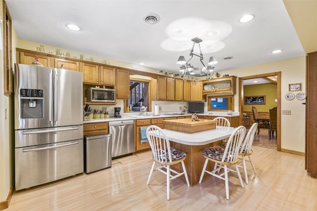 kitchen with pendant lighting, light hardwood / wood-style floors, appliances with stainless steel finishes, a notable chandelier, and a kitchen island