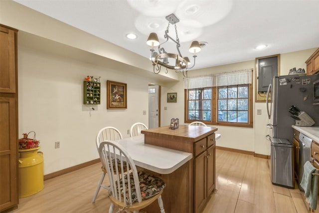 kitchen featuring light wood-type flooring, a kitchen island, a notable chandelier, stainless steel refrigerator, and hanging light fixtures