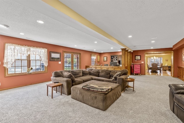 carpeted living room featuring french doors, a textured ceiling, and decorative columns