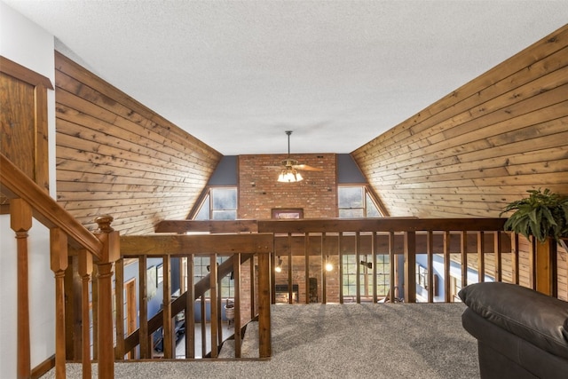 hall featuring carpet flooring, wooden walls, a textured ceiling, and lofted ceiling