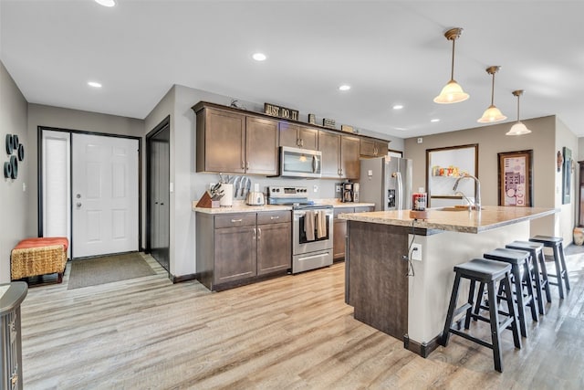 kitchen featuring light hardwood / wood-style flooring, pendant lighting, a center island with sink, and appliances with stainless steel finishes