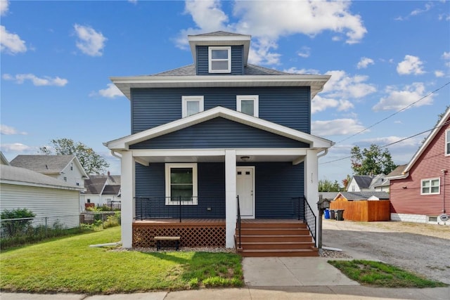 traditional style home with roof with shingles, a porch, a front yard, and fence