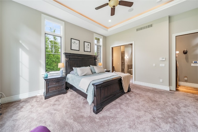 carpeted bedroom featuring a raised ceiling, ensuite bath, and ceiling fan