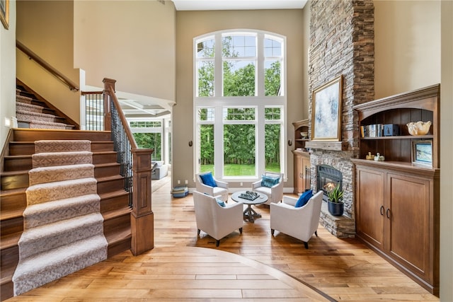 living room with a stone fireplace, a towering ceiling, and light hardwood / wood-style floors