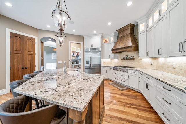 kitchen featuring custom exhaust hood, sink, a center island with sink, appliances with stainless steel finishes, and a breakfast bar area