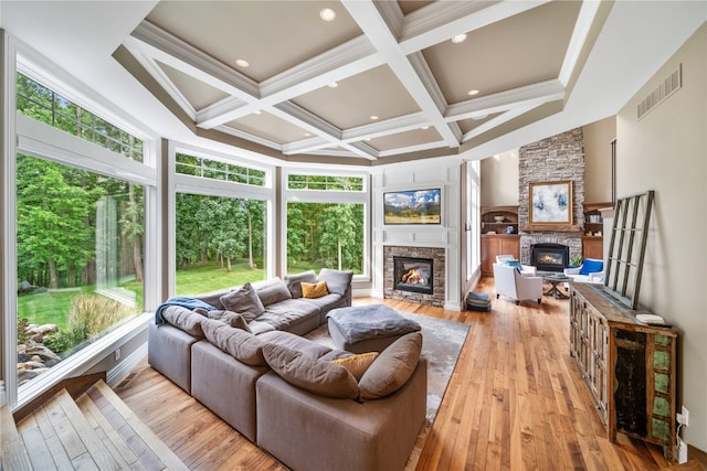 living room featuring light hardwood / wood-style floors, a stone fireplace, beam ceiling, and a wealth of natural light