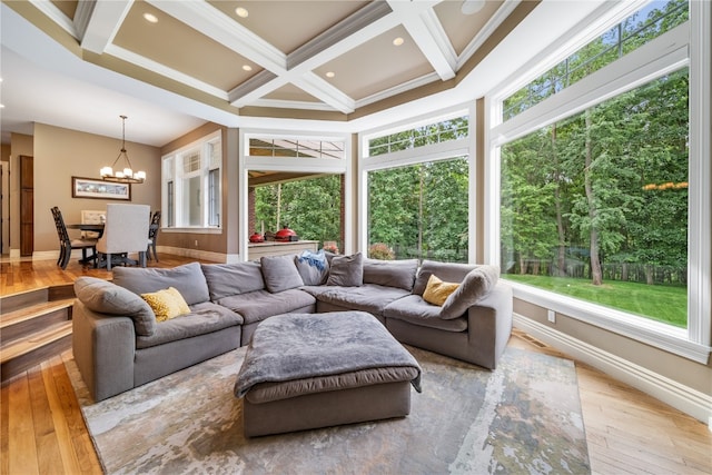 living room with beamed ceiling, coffered ceiling, light hardwood / wood-style flooring, an inviting chandelier, and crown molding