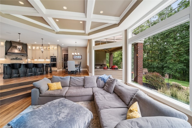 living room featuring hardwood / wood-style floors, coffered ceiling, ornamental molding, and an inviting chandelier