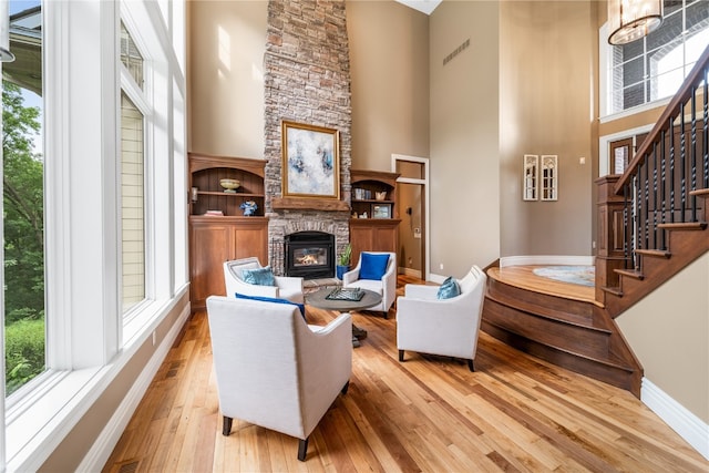 living area with a towering ceiling, a stone fireplace, light wood-type flooring, and plenty of natural light