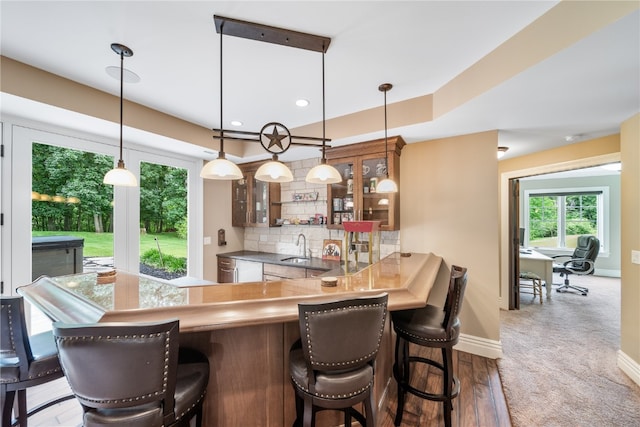 bar with backsplash, hanging light fixtures, dark wood-type flooring, and sink